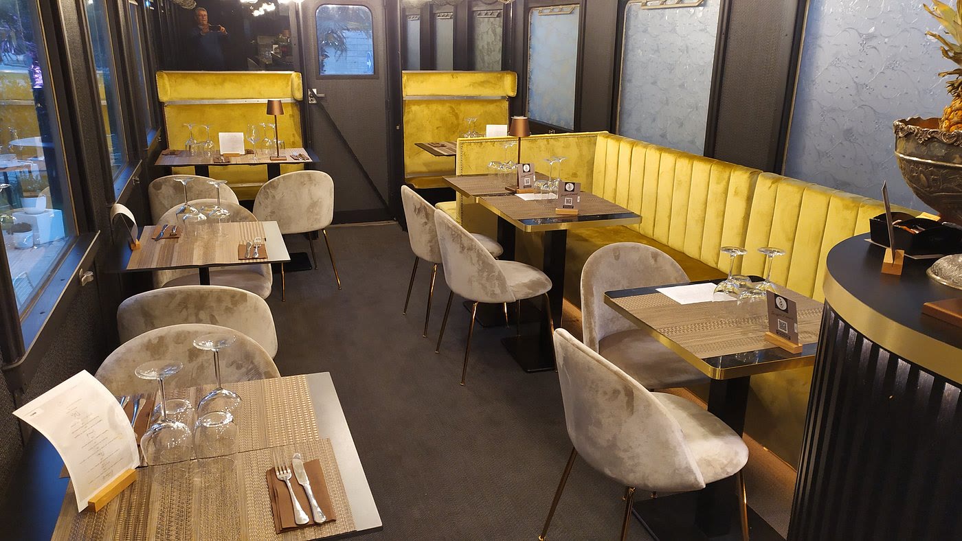 La sala della carrozza apparecchiata: divanetti di velluto oro, sedie grigie e i tavoli con i calici lungo i finestrini